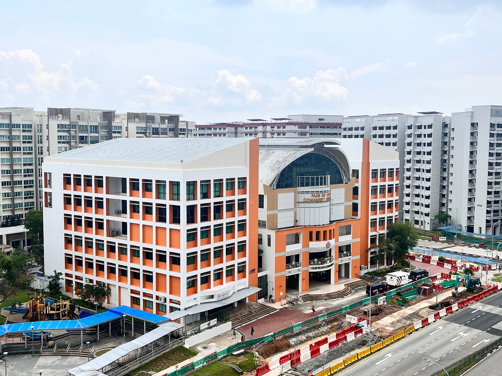 Daytime view of Pasir Ris East Community Club with orange and white facade, arched roof, and nearby HDB blocks